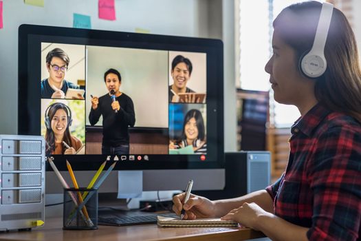 Closeup Asian woman hand writing lecture when online learning via video conference with teacher or speaker with colleague when Covid-19 pandemic, Coronavirus outbreak,online meeting,new normal concept