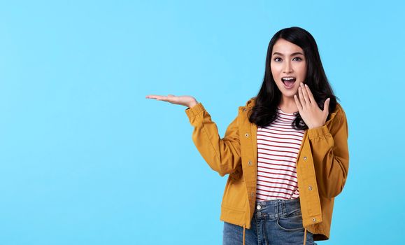 young asian woman gesture presenting an idea with hand open to copy space isolated on blue background.
