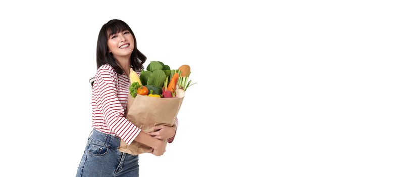 Happy smiling Asian woman holding paper shopping bag full of vegetables isolated on banner background with copy space.