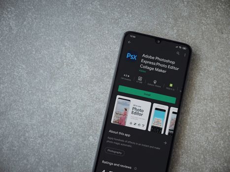 Lod, Israel - July 8, 2020: Adobe Photoshop Express Photo Editor app play store page on the display of a black mobile smartphone on ceramic stone background. Top view flat lay with copy space.