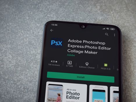 Lod, Israel - July 8, 2020: Adobe Photoshop Express Photo Editor app play store page on the display of a black mobile smartphone on ceramic stone background. Top view flat lay with copy space.
