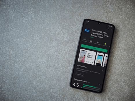 Lod, Israel - July 8, 2020: Adobe Photoshop Express Photo Editor app play store page on the display of a black mobile smartphone on ceramic stone background. Top view flat lay with copy space.
