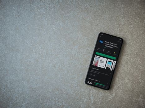 Lod, Israel - July 8, 2020: Adobe Photoshop Express Photo Editor app play store page on the display of a black mobile smartphone on ceramic stone background. Top view flat lay with copy space.