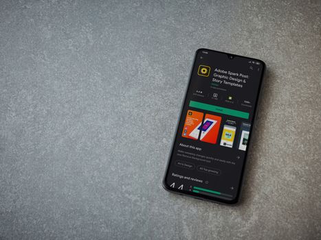 Lod, Israel - July 8, 2020: Adobe Spark Post - Graphic Design and Story Templates app play store page on the display of a black mobile smartphone on ceramic stone background.Top view flat lay with copy space