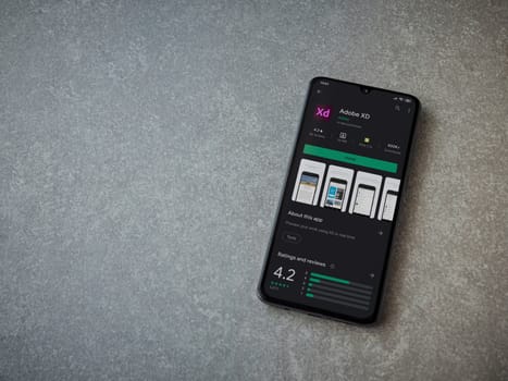Lod, Israel - July 8, 2020: Adobe XD app play store page on the display of a black mobile smartphone on ceramic stone background. Top view flat lay with copy space. 