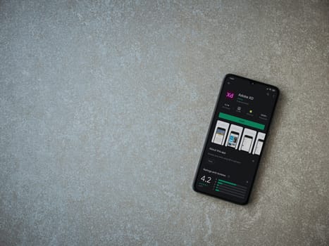 Lod, Israel - July 8, 2020: Adobe XD app play store page on the display of a black mobile smartphone on ceramic stone background. Top view flat lay with copy space. 