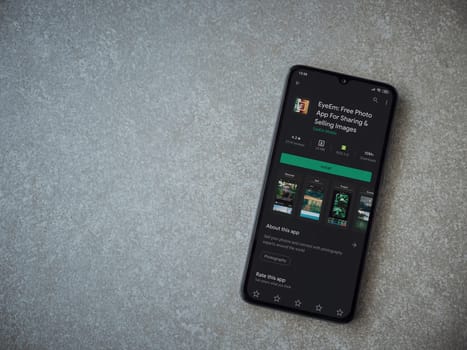 Lod, Israel - July 8, 2020: EyeEm - Sharing and Selling Images app play store page on the display of a black mobile smartphone on ceramic stone background. Top view flat lay with copy space.