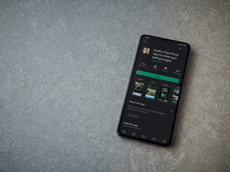 Lod, Israel - July 8, 2020: EyeEm - Sharing and Selling Images app play store page on the display of a black mobile smartphone on ceramic stone background. Top view flat lay with copy space.