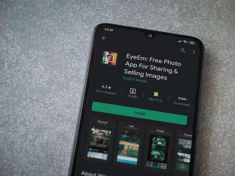 Lod, Israel - July 8, 2020: EyeEm - Sharing and Selling Images app play store page on the display of a black mobile smartphone on ceramic stone background. Top view flat lay with copy space.