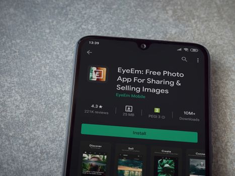 Lod, Israel - July 8, 2020: EyeEm - Sharing and Selling Images app play store page on the display of a black mobile smartphone on ceramic stone background. Top view flat lay with copy space.