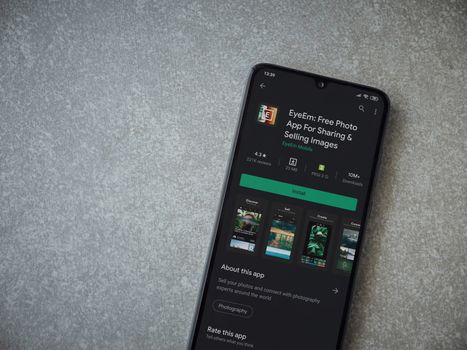 Lod, Israel - July 8, 2020: EyeEm - Sharing and Selling Images app play store page on the display of a black mobile smartphone on ceramic stone background. Top view flat lay with copy space.