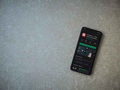 Lod, Israel - July 8, 2020: KineMaster - Video Editor and Movie Maker app play store page on the display of a black mobile smartphone on ceramic stone background. Top view flat lay with copy space.