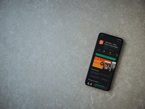 Lod, Israel - July 8, 2020: VivaVideo - Video Editor and Movie Maker app play store page on the display of a black mobile smartphone on ceramic stone background. Top view flat lay with copy space.