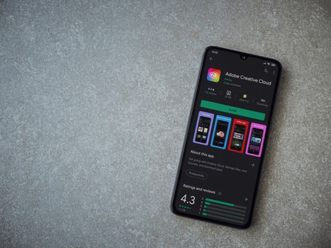 Lod, Israel - July 8, 2020: Adobe Creative Cloud app play store page on the display of a black mobile smartphone on ceramic stone background. Top view flat lay with copy space.