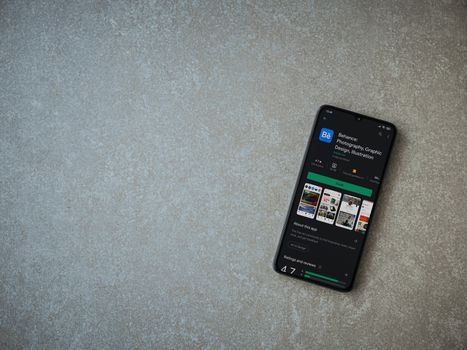 Lod, Israel - July 8, 2020: Adobe Behance app play store page on the display of a black mobile smartphone on ceramic stone background. Top view flat lay with copy space. 