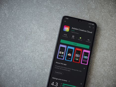 Lod, Israel - July 8, 2020: Adobe Creative Cloud app play store page on the display of a black mobile smartphone on ceramic stone background. Top view flat lay with copy space.