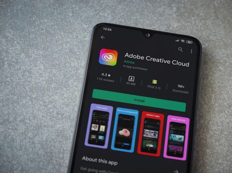 Lod, Israel - July 8, 2020: Adobe Creative Cloud app play store page on the display of a black mobile smartphone on ceramic stone background. Top view flat lay with copy space.