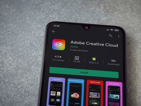 Lod, Israel - July 8, 2020: Adobe Creative Cloud app play store page on the display of a black mobile smartphone on ceramic stone background. Top view flat lay with copy space.