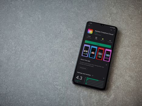 Lod, Israel - July 8, 2020: Adobe Creative Cloud app play store page on the display of a black mobile smartphone on ceramic stone background. Top view flat lay with copy space.
