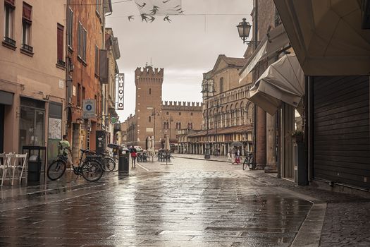 FERRARA, ITALY 29 JULY 2020 : Evocative view of the street that leads to Piazza Trento Trieste in Ferrara in Italy with people in their daily lives