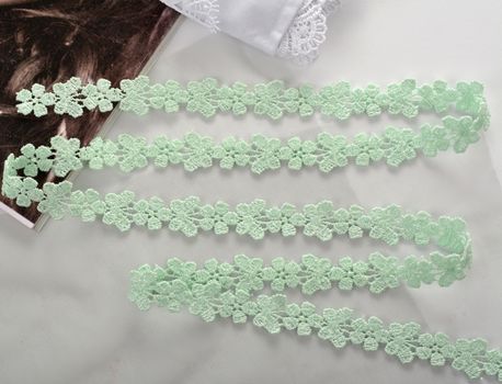 Tapes of green gentle guipure, beauty lace fabric on light background. Elastic material. Using for Atelier and needlework store.