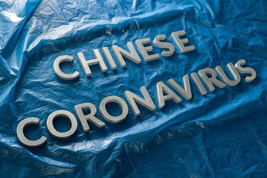 The words chinese coronavirus laid with silver metal letters on crumpled blue plastic film with diagonal perspective and selective focus. Pandemic flu concept,