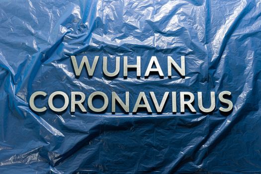 the words wuhan coronavirus laid with brushed silver metal letters on crumpled blue medical plastic film background - flat lay with centered composition and dramatic light