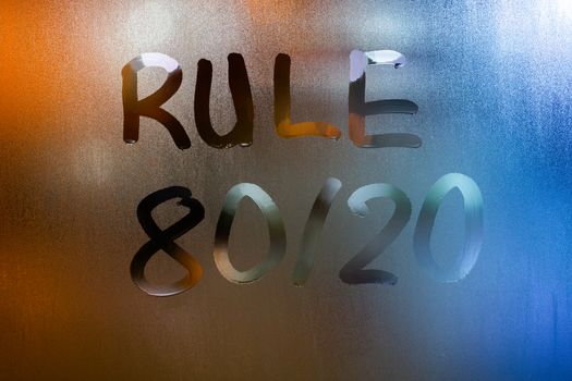 the phrase rule 80 by 20 - pareto principle - handwritten on classic blue night wet window glass with selective focus and blur