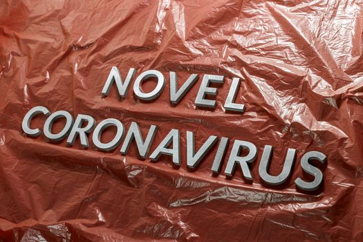 The words novel coronavirus laid with silver metal letters on emergency red crumpled plastic film with diagonal perspective, selective focus and dramatic light. Pandemic of chinese flu concept.