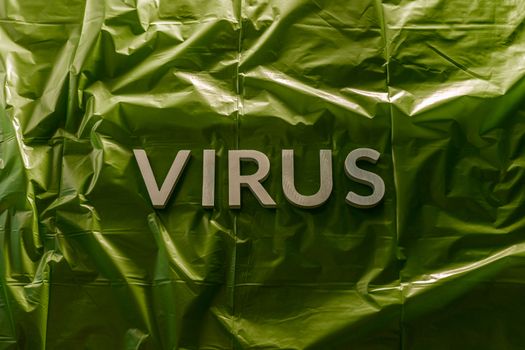 the word virus laid with brushed silver metal letters on green crumpled plastic film in horizontal centered composition and dramatic light