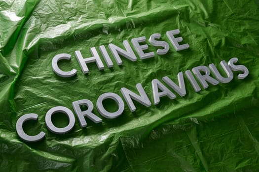 The words chinese coronavirus laid with silver metal letters on green crumpled plastic film with diagonal perspective and selective focus. Pandemic flu concept.