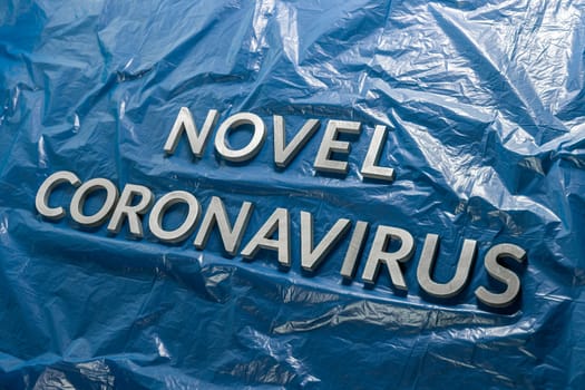 The words novel coronavirus laid with silver metal letters on crumpled blue plastic film with diagonal perspective and selective focus. Pandemic flu concept,