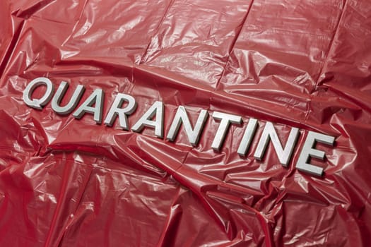 the word quarantine laid with silver letters on red crumpled plastic film surface in diagonal perspective and dramatic light