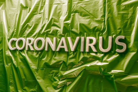 word coronavirus laid with silver letters on crumpled green plastic coat - in perstpective view with selective focus and dramatic cold light