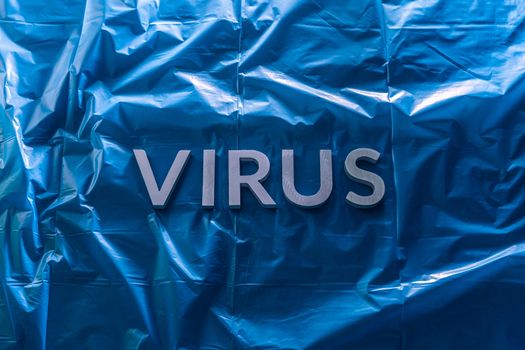 the word virus laid with brushed silver metal letters on crumpled blue plastic film in horizontal centered composition and dramatic light