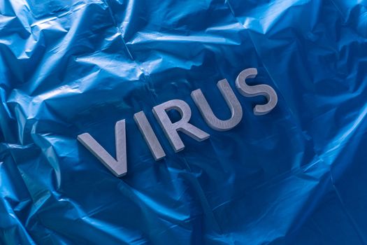 the word virus laid with brushed silver metal letters on crumpled blue plastic film diagonal perspective composition and dramatic light