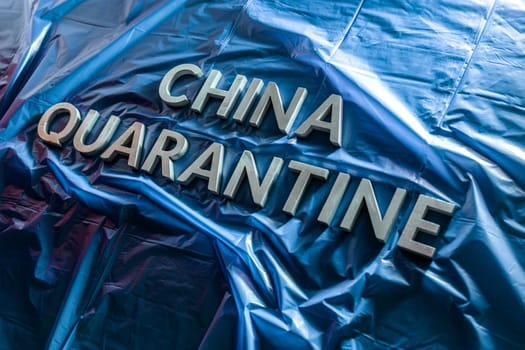 the words china quarantine laid with silver letters on crumpled blue plastic film in diagonal perspective and dramatic light
