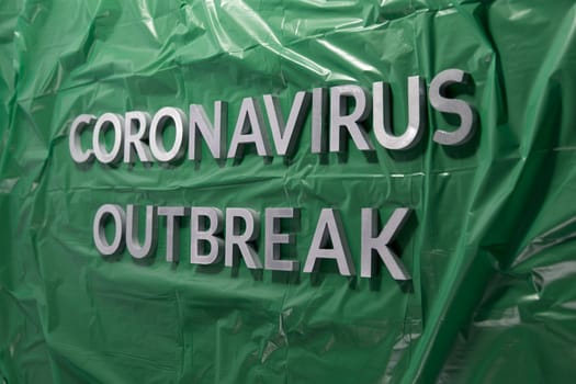 The words coronavirus outbreak laid with silver metal letters on green crumpled plastic film with perspective and selective focus. Pandemic flu concept.