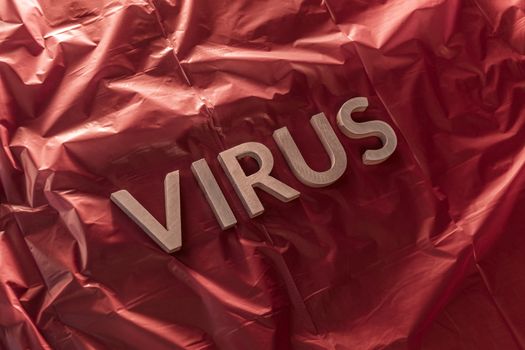the word virus laid with brushed silver metal letters on crumpled red plastic film diagonal perspective composition and dramatic light