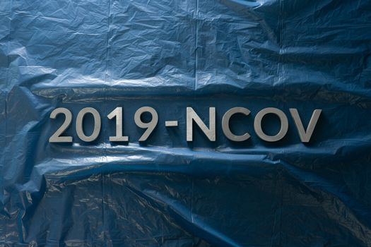 The word 2019-NCOV laid with metal letters on crumpled classic blue plastic film background in flat lay centered composition and dramatic light. Abstract chinese coronavirus concept,