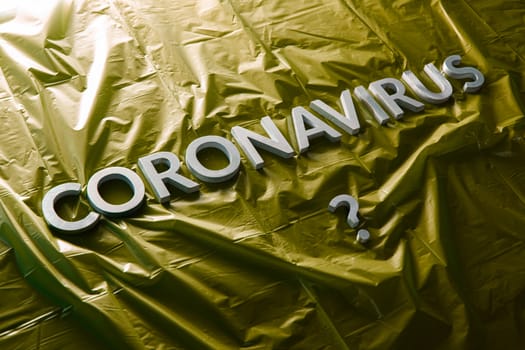 a question coronavirus laid with silver letters on crumpled yellow plastic film - diagonal composition with selective focus and dramatic light
