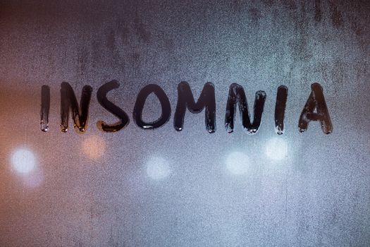 the word insomnia written on night wet window glass close-up with blurred background.