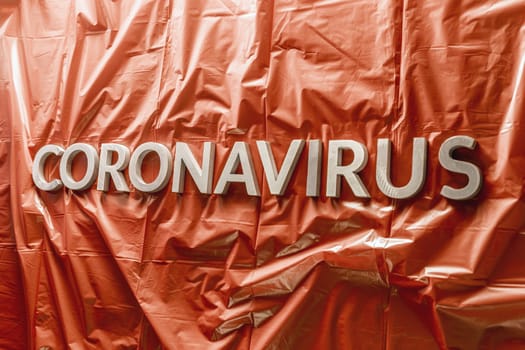 word coronavirus laid with silver letters on crumpled blue plastic coat - in perstpective view with selective focus and dramatic cold light