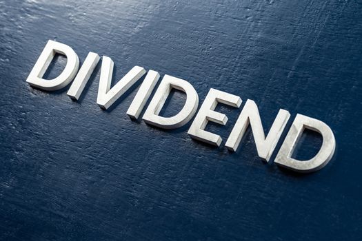 the word dividend laid by silver metal letters on gloss painted board background with selective focus in diagonal perspective