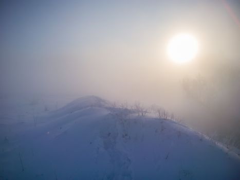 winter snow hill with footprints in deep snow at foggy morning.