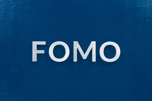 The abbreviation word fomo - fear of missing out - laid with silver letters on classic blue color flat painted surface. Stock market or crypto trading concept.