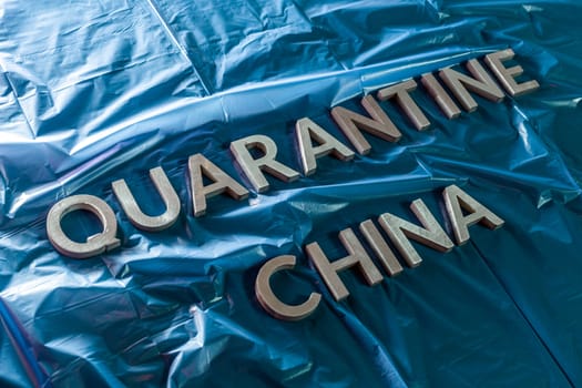 the words quarantine china laid with silver letters on crumpled blue plastic film in diagonal perspective and dramatic light