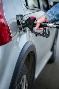 hand in jeans jacket refueling gray metallic car on gas station - closeup with selective focus and blur