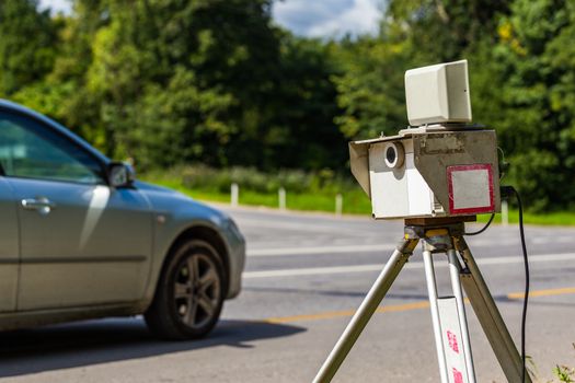 mobile speed camera device working on summer daytime road with blurry silver car in background - view from back