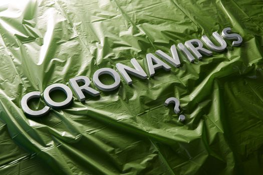 a question coronavirus laid with silver letters on crumpled green plastic film - diagonal composition with selective focus and dramatic light